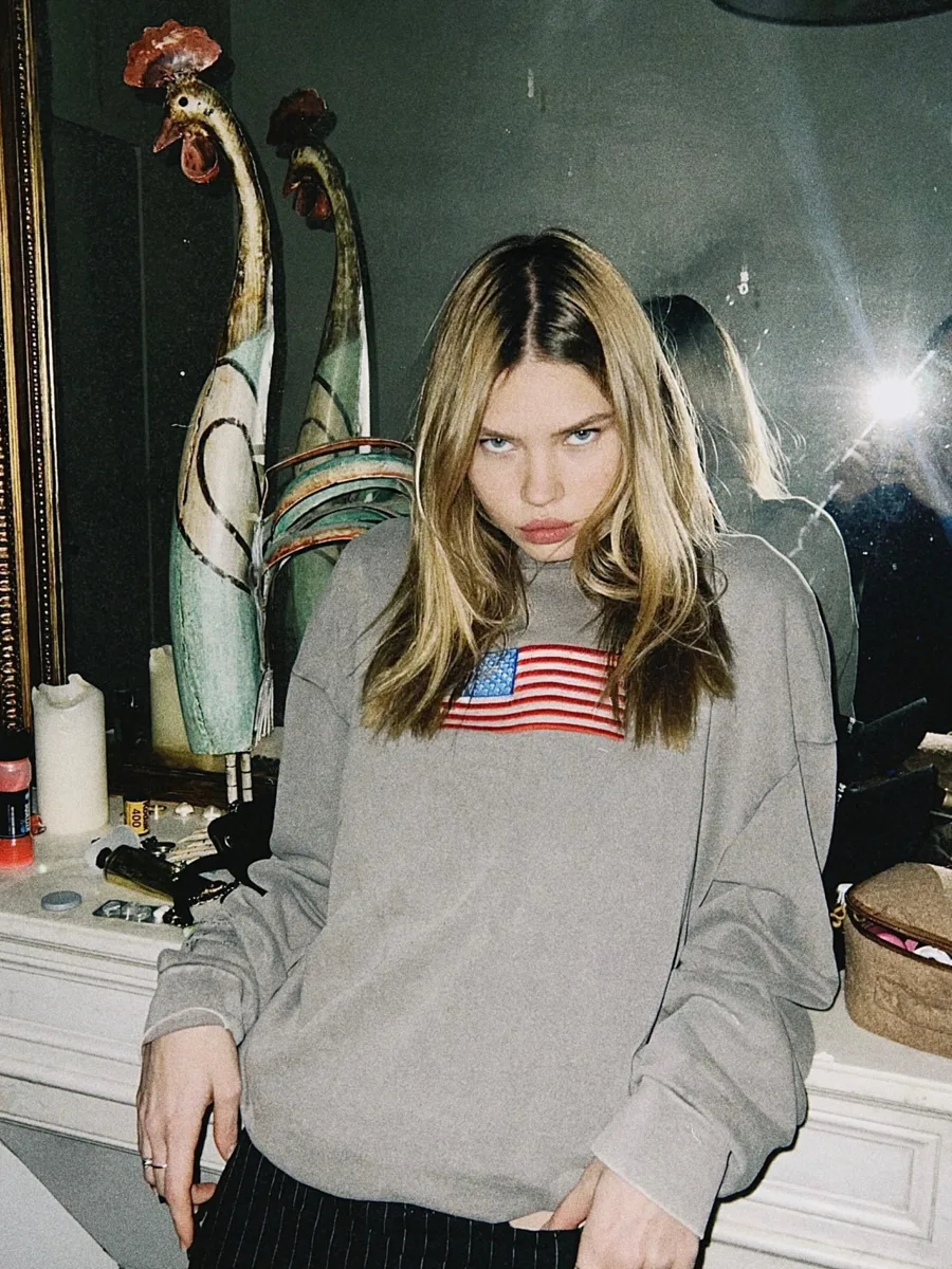 Model wearing a grey Dear America sweatshirt with an American flag