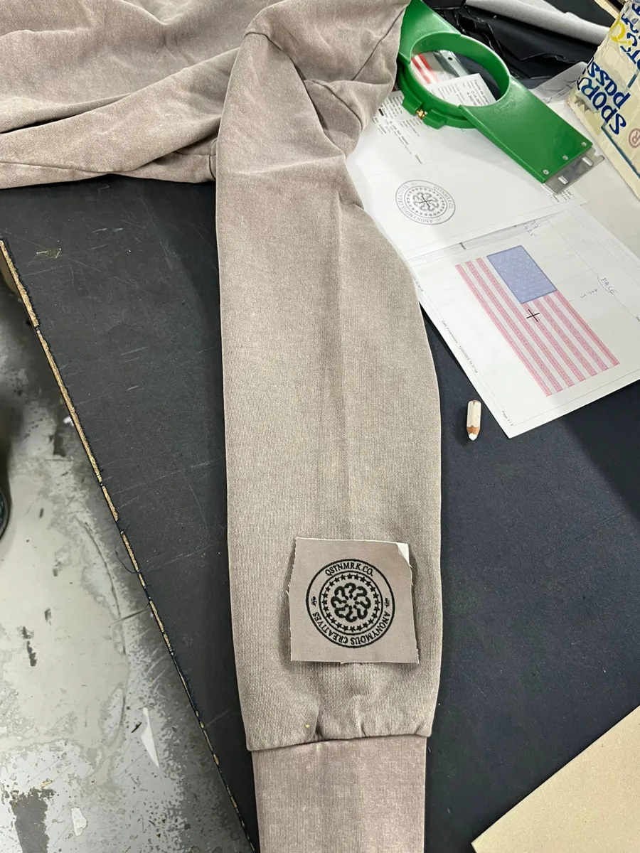 Beige sweatshirt with an embroidered seal patch beside flag prints